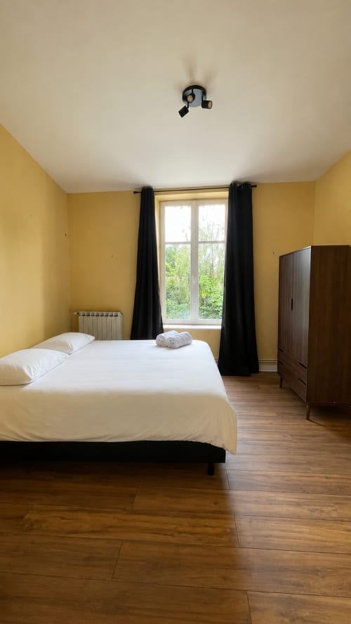 Chambre jaune vif avec lit blanc, armoire foncée et rideaux noirs au gîte Maison Agami à Rosières aux salins
