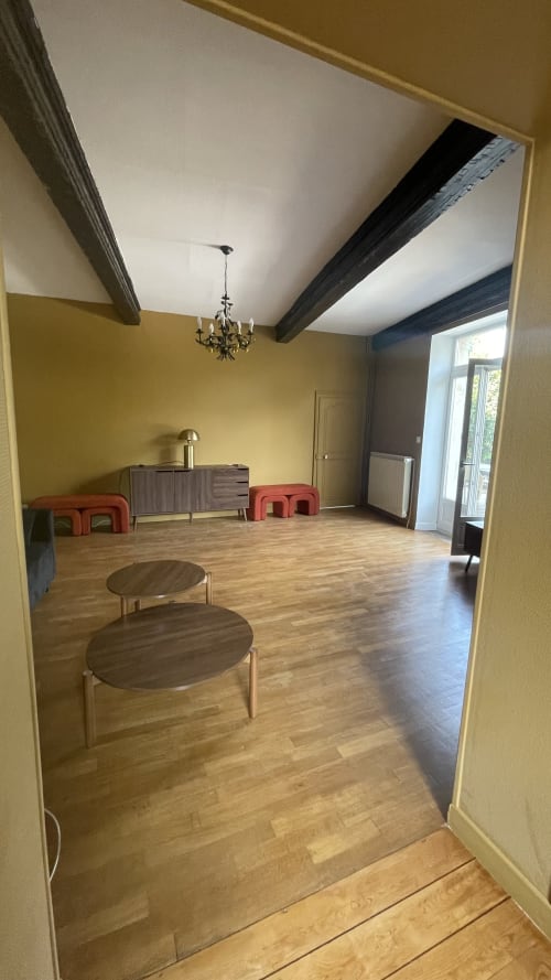 Spacieux séjour aux murs jaunes, poutres apparentes, parquet, sièges rouges et lustres du gîte Maison Agami.