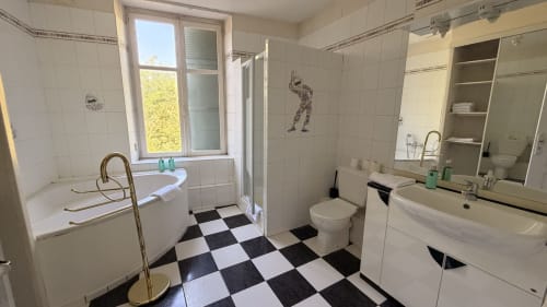 Spacieuse salle de bain carrelage noir et blanc, baignoire, lavabo, toilettes et douche au gîte Maison Agami
