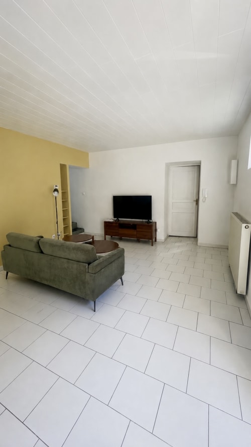 Salon moderne avec canapé vert, téléviseur et mur d'accent jaune à la Maison Agami à Rosières aux salines