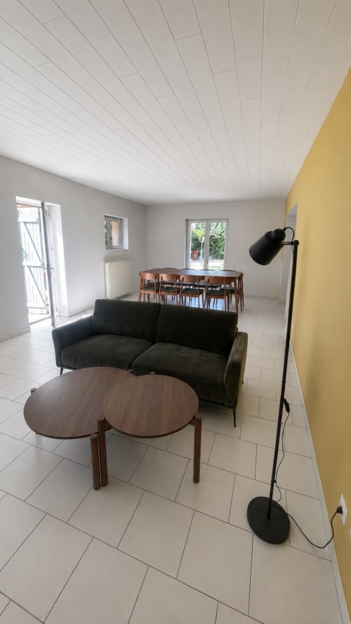 Salon moderne à la Maison Agami avec canapé noir courbe, table basse ronde en bois et mur d'accent jaune