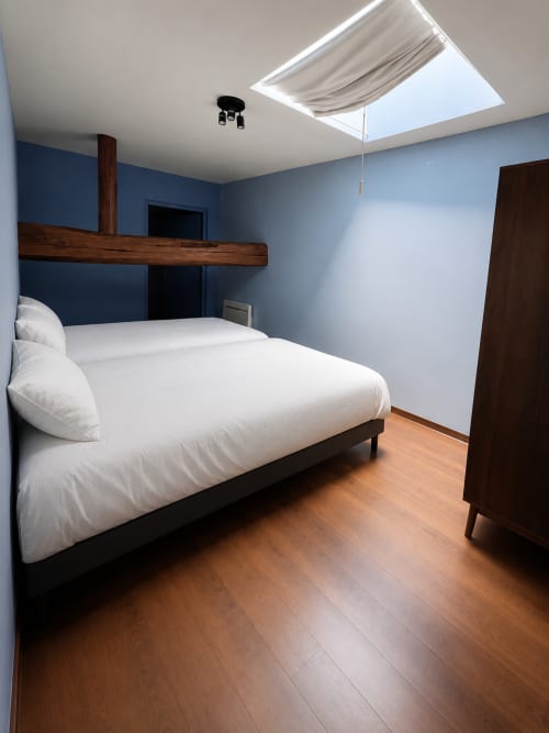 Chambre moderne de la Maison Agami avec lit queen-size, murs bleus, poutres en bois, puits de lumière et parquet