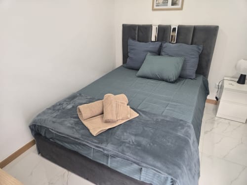 Quarto do Alojamento Boeing AL em Moreira da Maia com cama cinza, almofadas, toalhas dobradas e criado branco