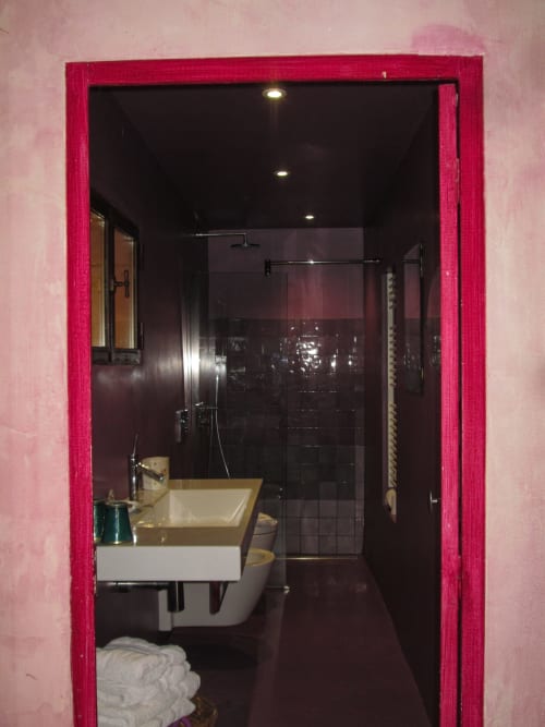 Modern bathroom at Clos Bb with pink walls, black tile shower, vessel sink, and recessed lighting