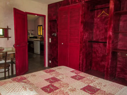 Bright bedroom at Clos B&B in Saint-Cyr sur Mer with red velvet doors, patterned bedding, and wooden furniture