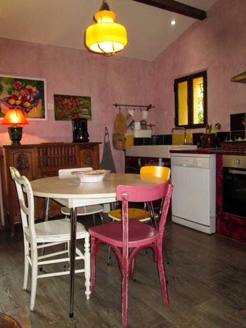 Colorful retro kitchen and dining area at Clos Bb in Saint-Cyr sur Mer with pink walls, vintage chairs, and yellow pendant