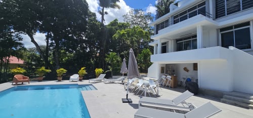 Zone piscine de la Villa Les Cassias avec transats, parasol et bâtiment blanc moderne à Petit Bourg, Guadeloupe