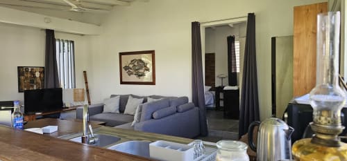 Spacieux séjour de la villa Les Cassias avec canapé gris, kitchenette, TV et accès à la chambre par rideaux