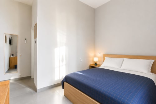 Camera moderna a Darna Rooms a Napoli con letto in legno, cuscini bianchi, coperta trapuntata blu navy e luminosa luce naturale