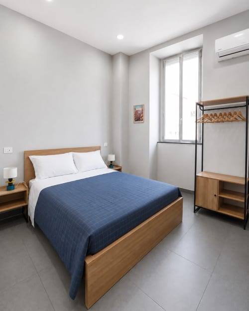 Camera moderna a Darna Rooms, Napoli. Letto matrimoniale con coperta trapuntata blu, arredamento in legno, aria condizionata e finestre a tutta altezza