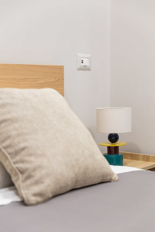 Camera moderna presso Darna Rooms Napoli con letto in legno, biancheria bianca, lampada sul comodino e presa murale