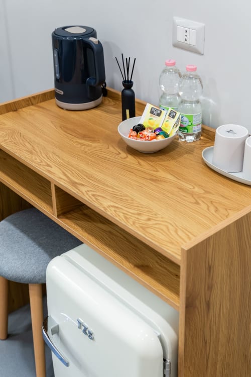 Scrivania in legno presso Darna Rooms Napoli con bollitore, diffusore, bottiglie d'acqua, snack e minibar sottostante