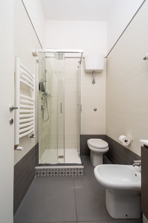Bagno moderno presso Darna Rooms Napoli con doccia, wc, lavabo su colonna e rivestimenti in piastrelle scure