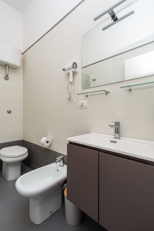 Bagno moderno presso Darna Rooms Napoli con piastrelle bianche, pavimento scuro, lavabo, WC, bidet, specchio e servizi