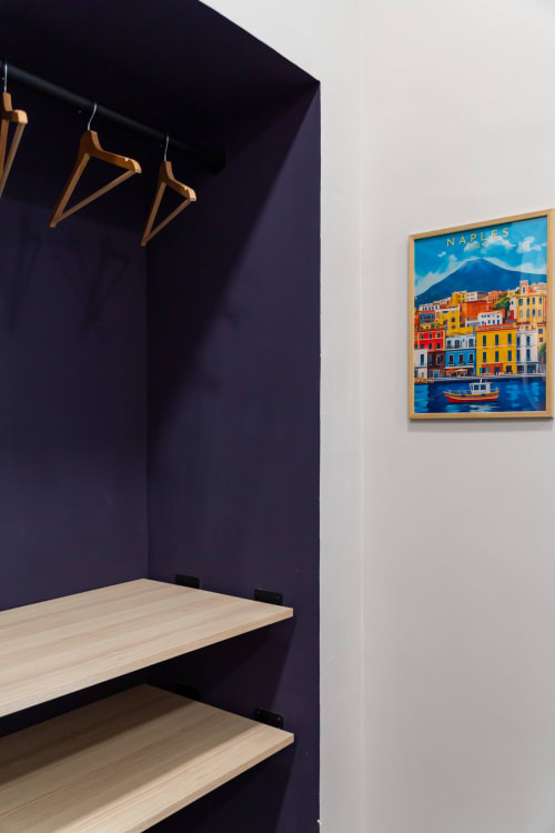 Moderna nicchia guardaroba con appendiabiti in legno e scaffali, manifesto di viaggio Napoli su parete bianca a Darna Rooms