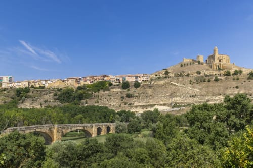 Puente de piedra histórico sobre río con el pueblo de San Vicente de la Sonsierra y catedral en la ladera, España