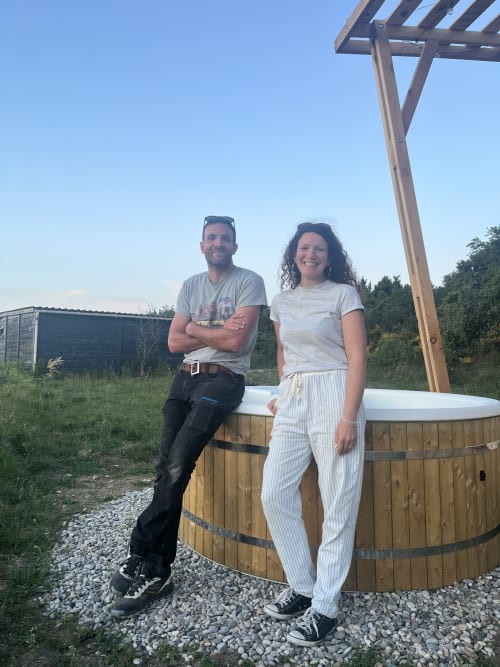 Couple posing by wooden hot tub at Pépite BnB in Villeneuve, France with pergola overhead