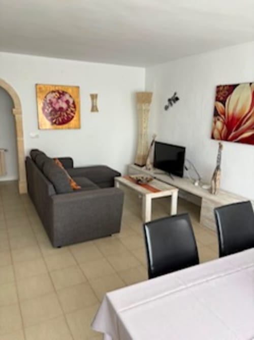 Sala de la Suite No. 1 de Casa Marina Suites con sillón gris, televisor de pantalla plana, sillas de comedor y cuadros florales
