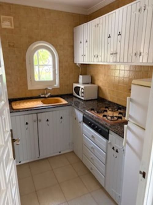 Cocina compacta en suite de Casa Marina Suites con gabinetes blancos, estufa a gas, ventana arqueada y encimeras de madera