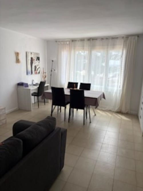 Suite moderna en Casa Marina con mesa de comedor, sillas negras, sofá, escritorio y vista al mar a través de amplios ventanales con cortinas
