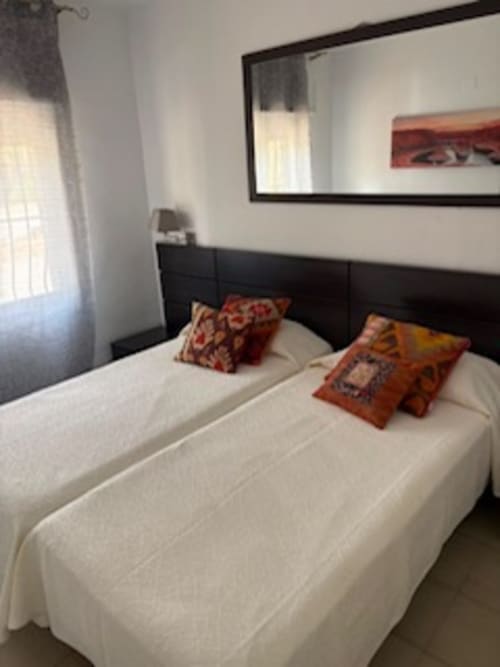 Dormitorio moderno en Casa Marina Suites con dos camas, almohadas decorativas, cabecero oscuro, espejo y ventana con vistas al mar