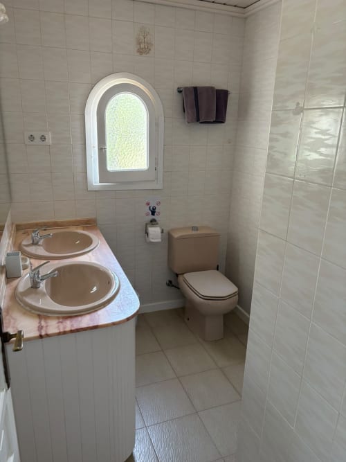 Baño moderno en suite de Casa Marina Suites con doble lavabo, inodoro, ventana arqueada, paredes alicatadas y zona de ducha.