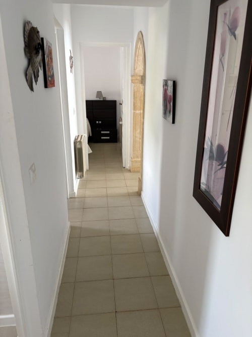 Pasillo en Casa Marina Suites, casa de huéspedes española con piso de azulejos, paredes blancas y cuadros enmarcados