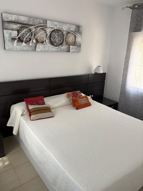 Habitación moderna en Casa Marina Suites con ropa de cama blanca, cabecero negro, arte decorativo en la pared y almohadas coloridas