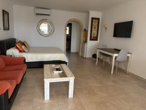 Suite 2 de Casa Marina Suites con sofá rojo, cama, TV, escritorio y balcón con vista a la piscina en hotel español