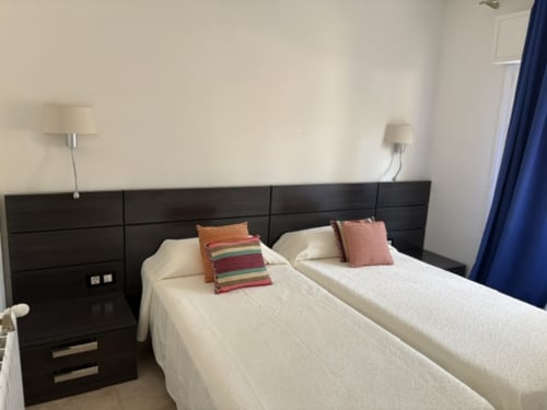 Moderno dormitorio de hotel en Casa Marina Suites con camas gemelas, cabecero oscuro y cortinas azules