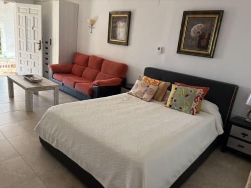 Suite 2 Casa Marina Suites con cama queen, sofá rojo, cuadros enmarcados y vista a la piscina en propiedad frente al mar