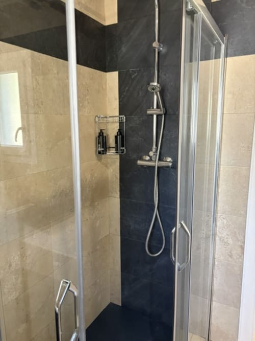 Moderna cabina de ducha con pared de acento negro y azulejos beige en el baño de la suite Casa Marina Suites