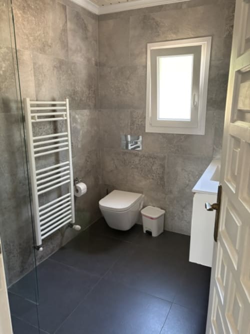 Baño moderno en Casa Marina Suites con paredes de azulejos grises, toallero calefactable montado en pared, inodoro suspendido y decoración oscura