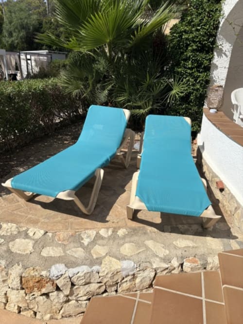 Dos cómodas sillas reclinables azules en la terraza de Casa Marina Suites, propiedad frente al mar con palmeras y patio de piedra
