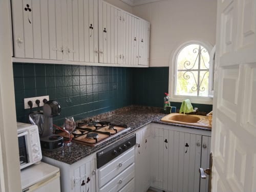 Cocina compacta en apartamento Casa Marina Suites con muebles blancos, azulejo verde azulado oscuro, encimera de granito, estufa a gas
