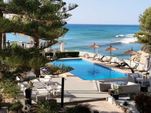 Piscina frente al mar de Casa Marina Suites con vistas al Mediterráneo, tumbonas, sombrillas y pinos en España