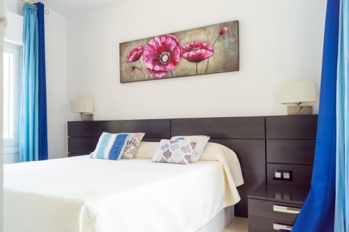 Suite de 6 dormitorios Casa Marina Suites con cabecero oscuro, ropa de cama blanca, arte de amapolas rosas, cortinas azules y vista al mar