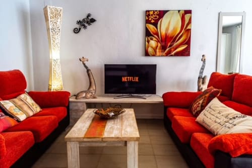 Sala de estar de la Suite 6 de Casa Marina Suites con sofás rojos, mesa de madera, TV de pantalla plana y arte mural colorido en España