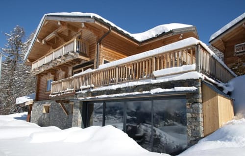 Villa alpine enneigée aux Chalets d'Aline avec architecture bois, soubassement en pierre et vue sur les montagnes en France
