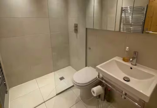 Salle de bain moderne et épurée de la villa Les Chalets d'Aline avec carrelage blanc, toilettes, lavabo et douche à La Plagne