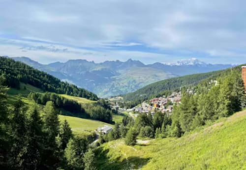 Vue panoramique de la vallée alpine avec prairies verdoyantes, forêts et pics montagneux près de la station de ski La Plagne Tarentaise