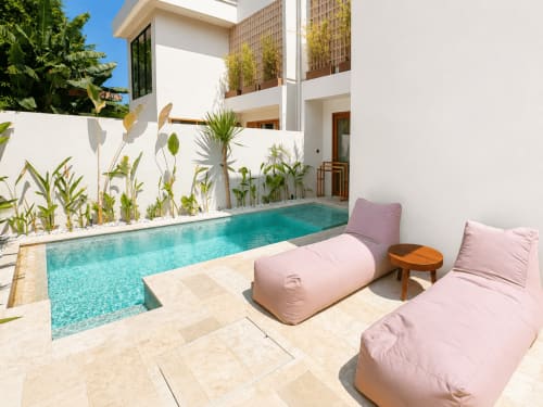 Piscina privada de Oasis Dune Villas con agua turquesa, tumbonas rosas, plantas tropicales y villa moderna blanca