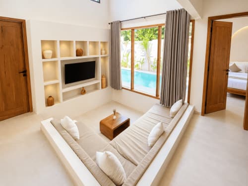 Sala de estar de lujo en Oasis Dune Villas con asientos hundidos, TV, vista a piscina y detalles modernos en madera
