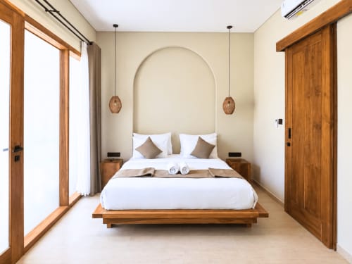 Habitación moderna en Oasis Dune Villas Lombok con cama de plataforma de madera, cabecero arqueado, lámparas colgantes y decoración minimalista