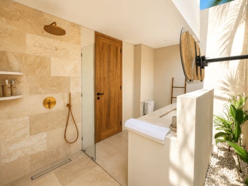 Baño moderno en Oasis Dune Villas con ducha tropical, puerta de madera, azulejos de piedra y plantas exóticas en Lombok