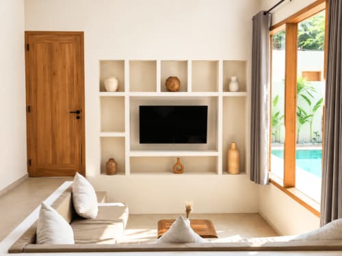 Modern villa living room at Oasis Dune Villas with TV wall unit, white sofas, wooden doors, and pool view in Lombok