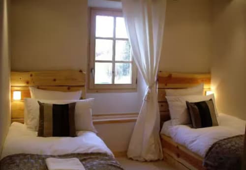 Chambre twin aux Chalets d'Aline avec lits jumeaux, oreillers blancs, coussins rayés, têtes de lit en bois, fenêtre blanche