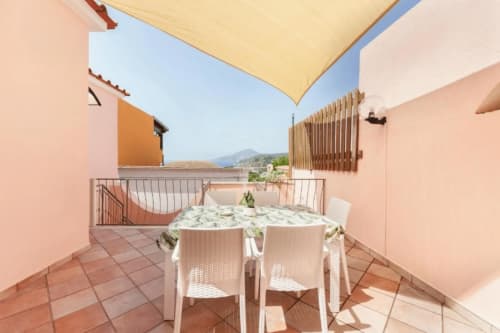 Terrazza soleggiata di Origenes Rooms Procida con tavolo da pranzo, ombrellone giallo e vista sul mare