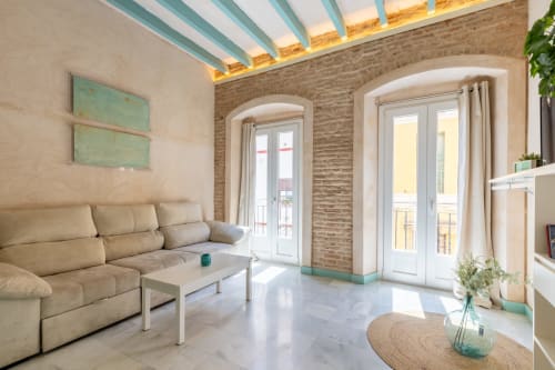 Salón moderno en apartamento de Triana, Sevilla con sofá beige, ladrillo visto, puertas arqueadas, claraboya y vistas a la ciudad
