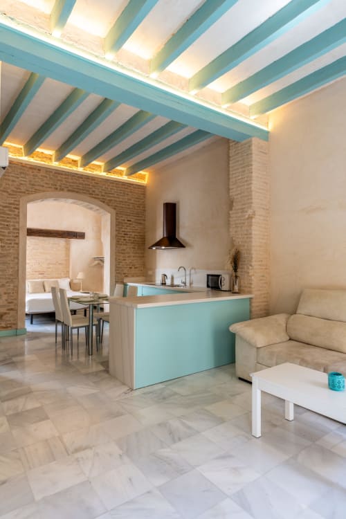 Apartamento moderno en Sevilla con viga turquesa en techo, cocina americana, comedor y sofá beige en espacio abierto